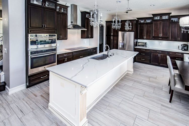 Modern kitchen with dark wood cabinets, white island, stainless appliances, and light gray flooring