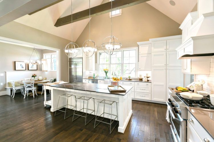 Bright modern kitchen with white cabinetry, large island, pendant lights, and dark wood floors
