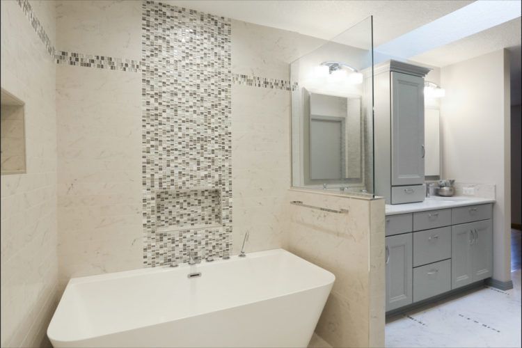 Modern bathroom with freestanding tub, mosaic tile accent wall, and double vanity under bright lighting