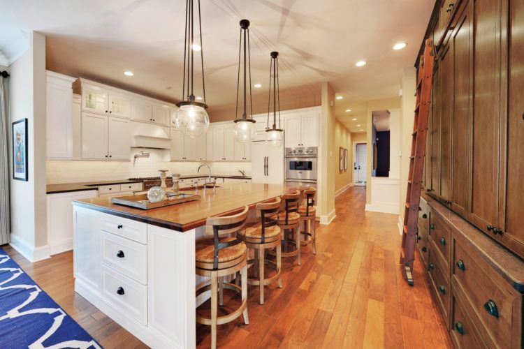 Bright kitchen with large island, pendant lights, wood floors, and a hallway beside built-in cabinets