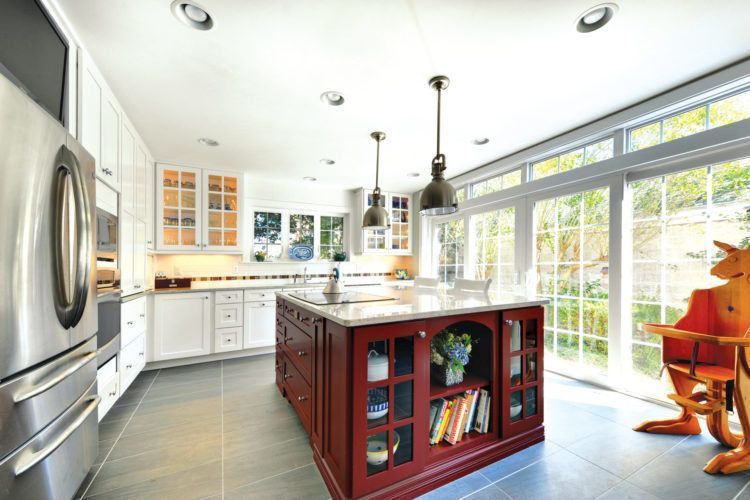 Bright modern kitchen with white cabinets, red island, stainless fridge, and large windows looking outside