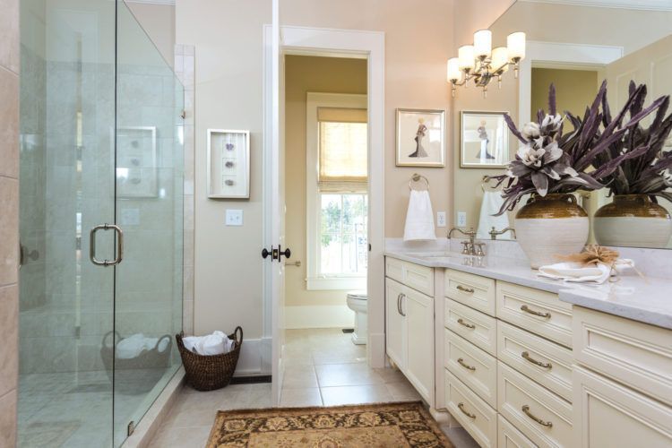 Bright bathroom with glass shower, double vanity, and a vase of flowers on the counter.