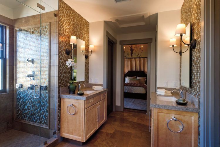 Luxury bathroom with double vanities, glass shower, warm lighting, and stone tile accents
