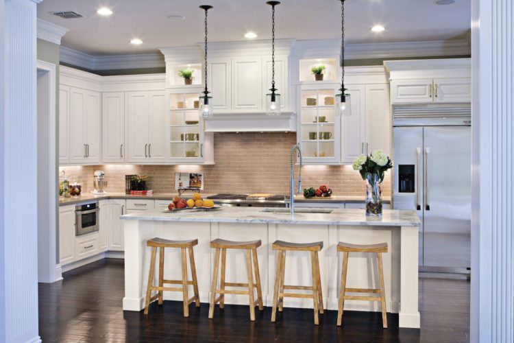 Bright white kitchen with island, wood stools, pendant lights, and dark floors