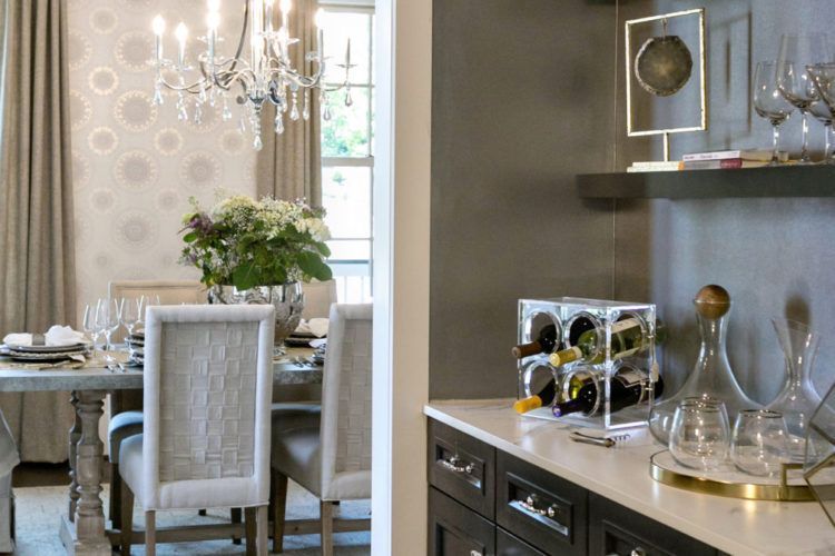 Elegant dining room with chandelier, upholstered chairs, and a console displaying glassware and decor