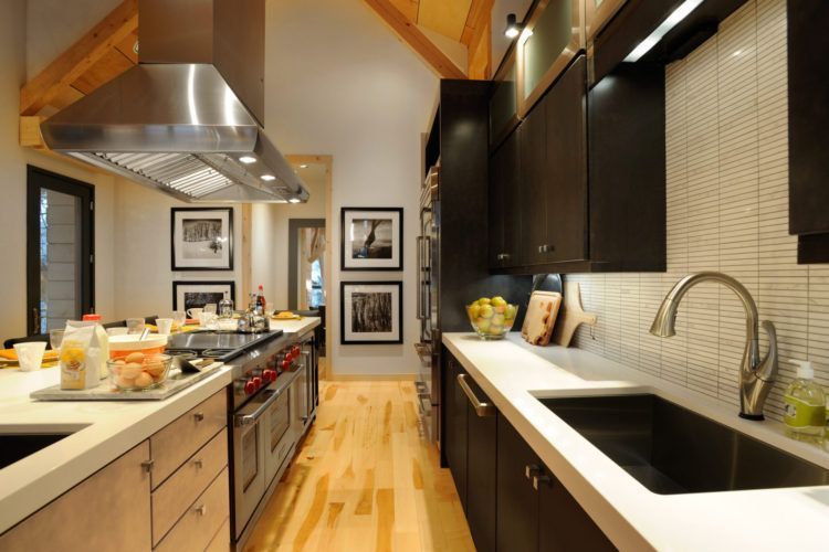 Modern galley kitchen with wood beams, dark cabinets, stainless range hood, and a light countertop if