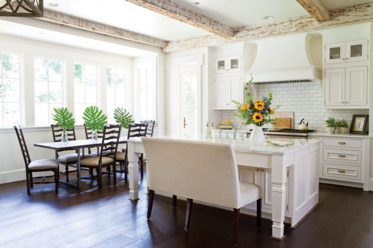 Bright white kitchen and dining area with dark wood floors, island, and table by windows with potted plants.