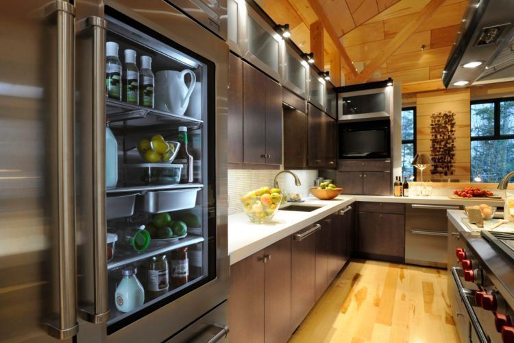 Modern kitchen with dark wood cabinets, stainless appliances, and a built-in glass-door fridge stocked with drinks.
