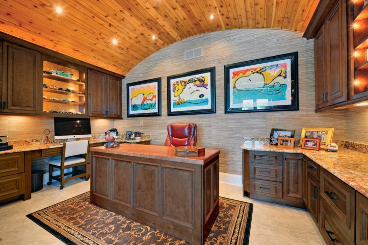 Wood-paneled home office with large desk, bookshelves, and colorful framed artwork on the wall