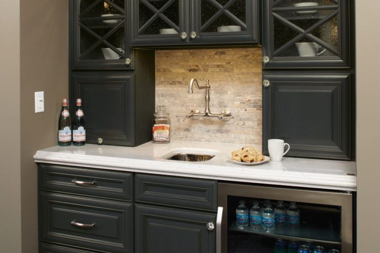 Black kitchen bar with white countertop, sink, glass backsplash, and bottles and cups on the counter
