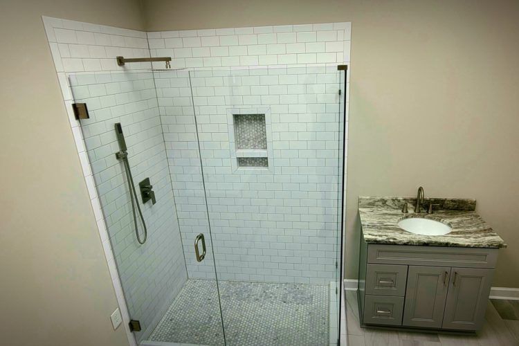 Accessible walk-in shower with tiled walls and built-in niche beside a small granite vanity.