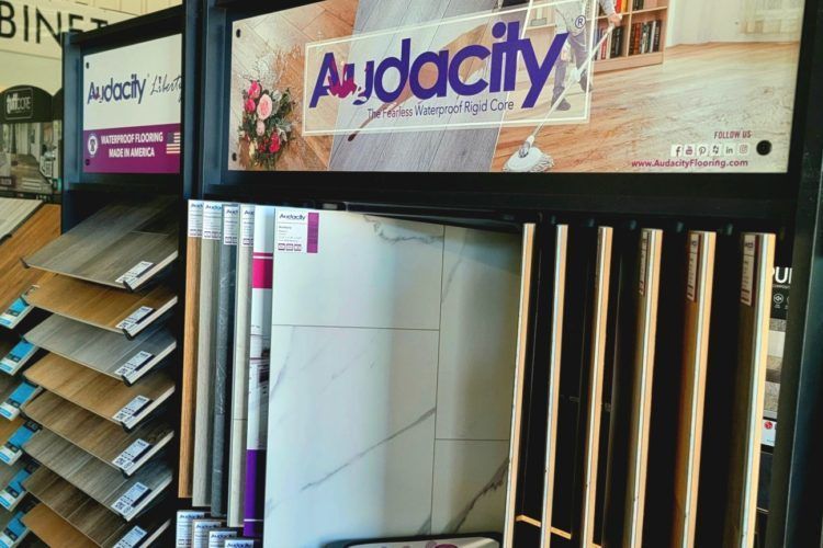 Display of Audacity door samples and panels in a showroom, with logo signs and stacked materials.