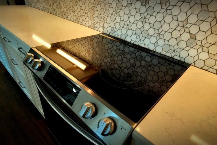 Modern kitchen stovetop with stainless steel knobs and black glass cooktop against hexagon tile backsplash