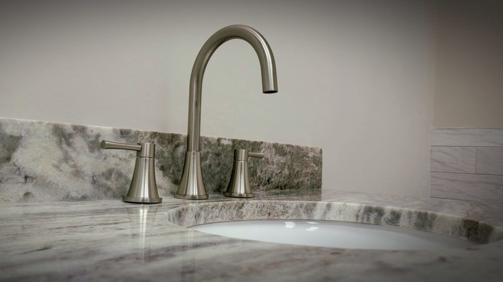 Chrome faucet over a white marble bathroom sink with gray veining