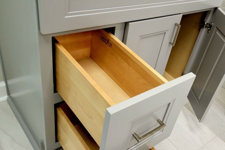 Open kitchen drawer with a wooden interior and white front panel, partially pulled out from gray cabinetry