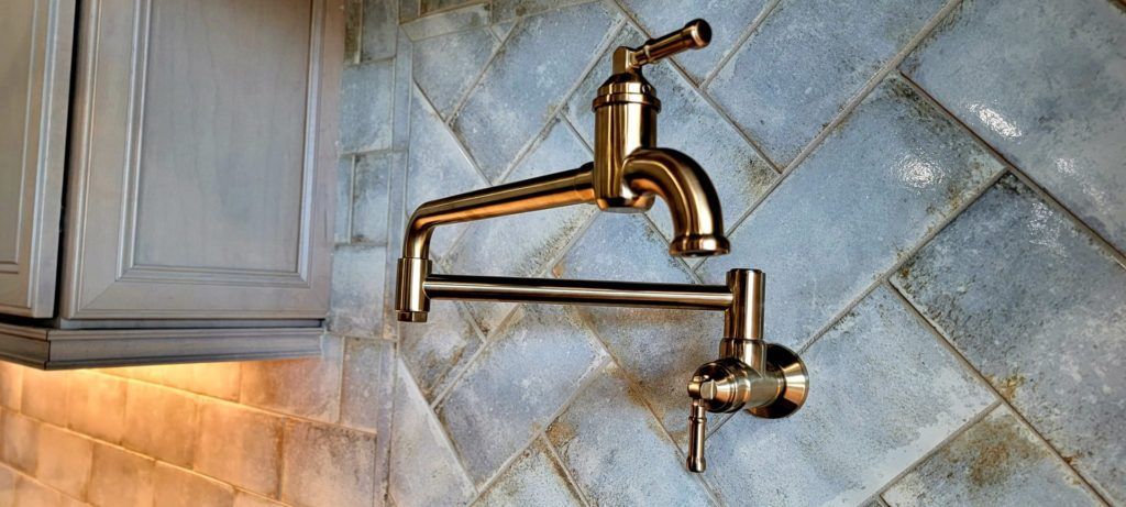 Brass wall-mounted pot filler faucet over a tiled kitchen backsplash