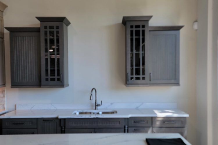 Modern gray kitchen with cabinets, sink, and white countertops against a beige wall
