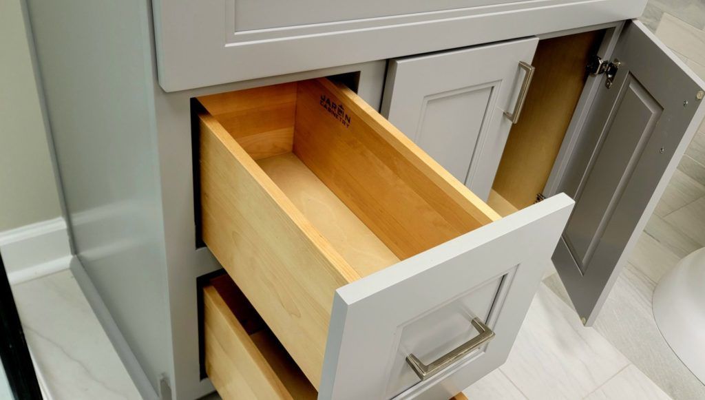 Open drawer in a gray kitchen cabinet, showing a light wood interior.