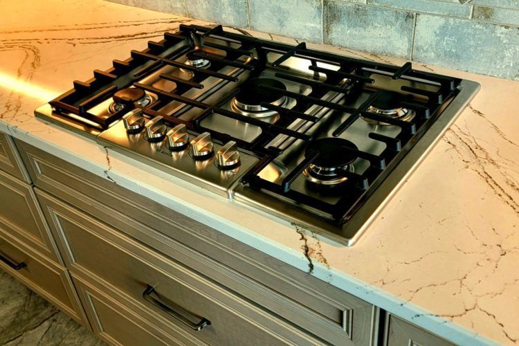 Black gas cooktop with stainless knobs on a white marble kitchen counter