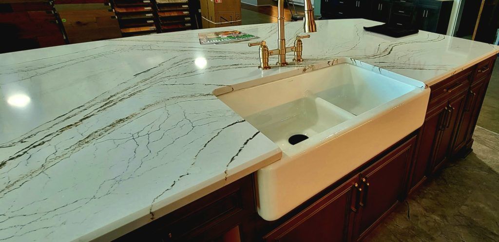 Kitchen island with marble countertop and white farmhouse sink, set against dark wood cabinets.