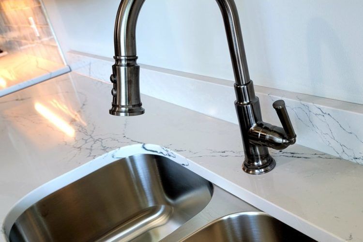 Chrome kitchen faucet over stainless steel sink and light marble countertop.