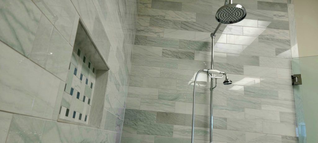 Modern tiled shower with rain showerhead and handheld sprayer, gray and white stone walls.