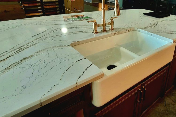 White marble kitchen countertop with integrated white sink and gold faucet over dark wood cabinets