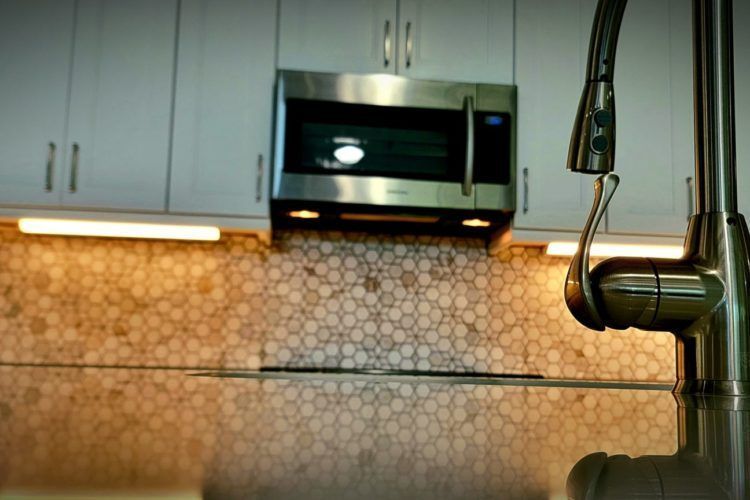Modern kitchen with white cabinets, stainless microwave, mosaic tile backsplash, and chrome faucet