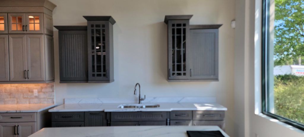 Modern kitchen with white walls, dark cabinets, stainless sink, and a large window overlooking greenery