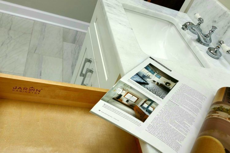 Open magazine on a bathroom counter beside a sink and wooden tub, showing a modern interior design spread