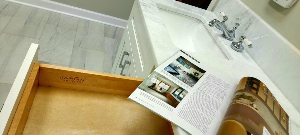 Open book on a bathroom counter beside a sink and an open drawer.