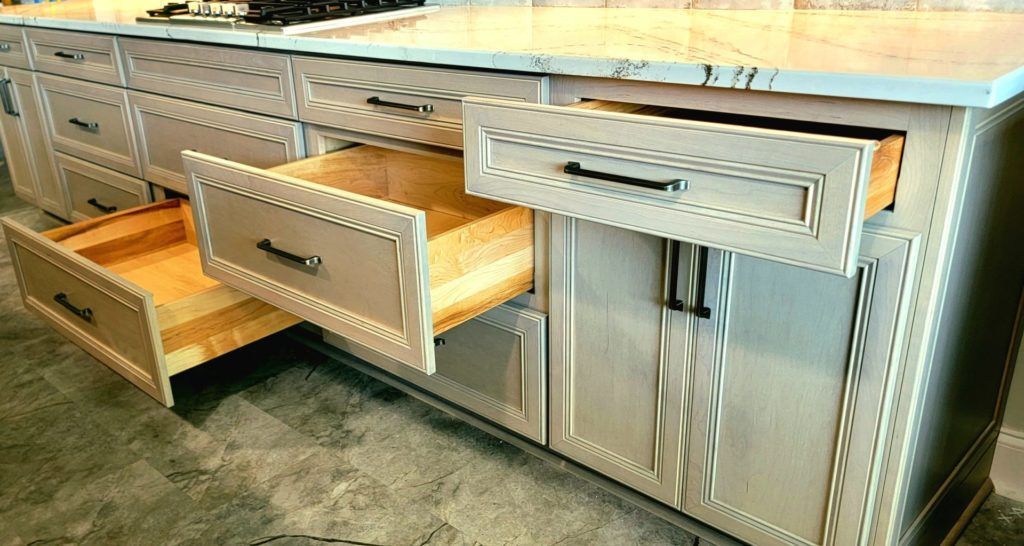 Silver kitchen cabinets with multiple open drawers, including a wooden utensil drawer and a pull-out shelf.