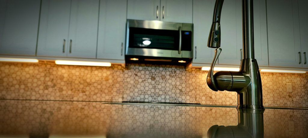 Modern kitchen with cabinets, tiled backsplash, microwave, and a faucet in the foreground