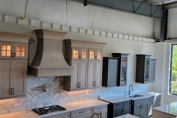 Bright modern kitchen with white cabinets, marble backsplash, black range hood, and large windows