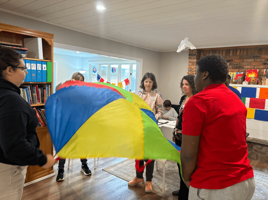 A group of people are playing with a colorful parachute in a living room.