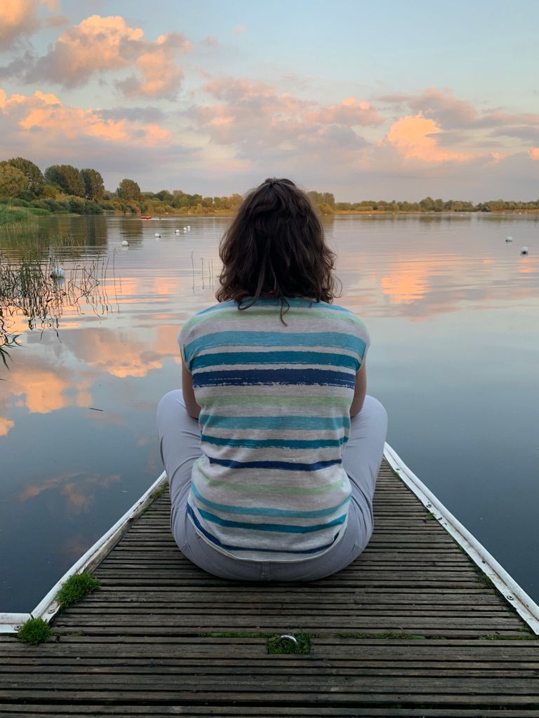 photo of a person sitting on a pier, looking out over a lake and a beautiful cloud sky