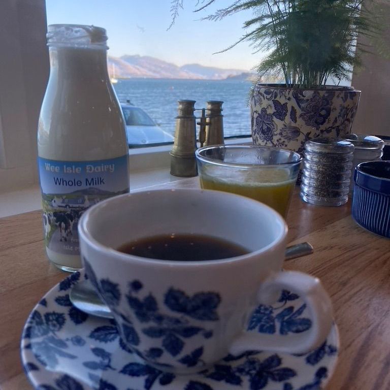 photo of a coffee and milk on a table with a view through the window of lake and mountain