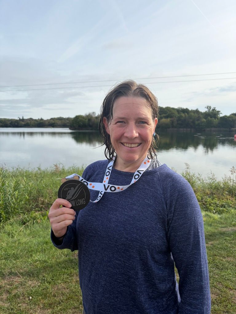 photo of a lady by a lake with wet hair holding a medal