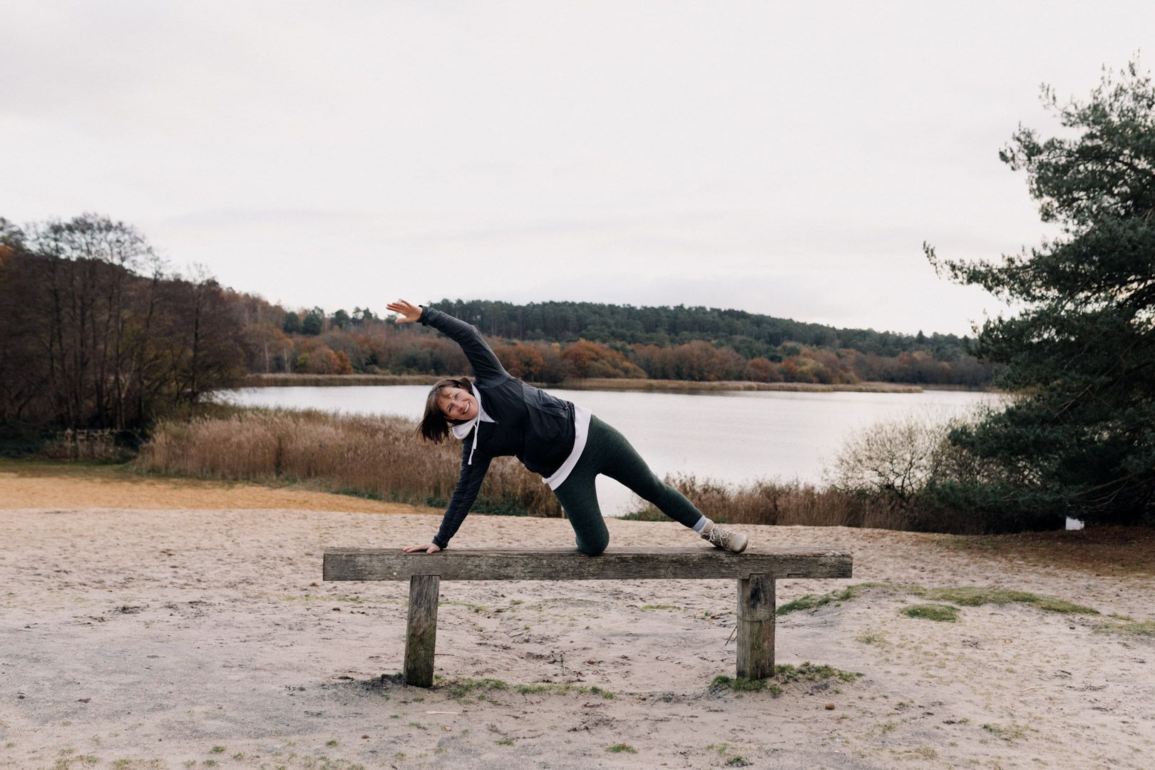 photo of a lady on a bench doing a kneeling side stretch with trees and a lake behind