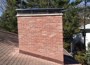 A brick chimney on top of a roof with trees in the background.