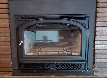 A black fireplace with a brick wall in the background.