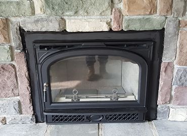 A fireplace with a black door and a stone wall behind it.