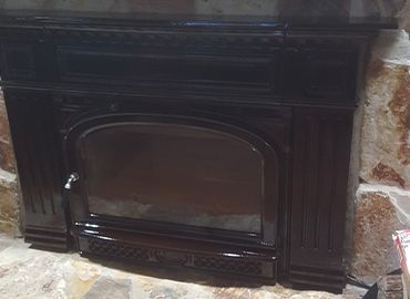 A black fireplace is sitting in a stone fireplace.