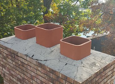 Three brick chimneys are sitting on top of a brick chimney.