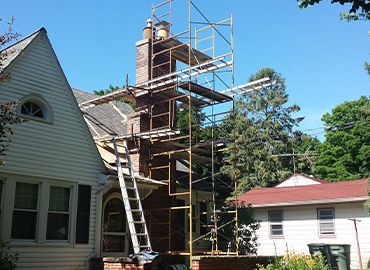 A chimney is being repaired in front of a house with scaffolding around it.