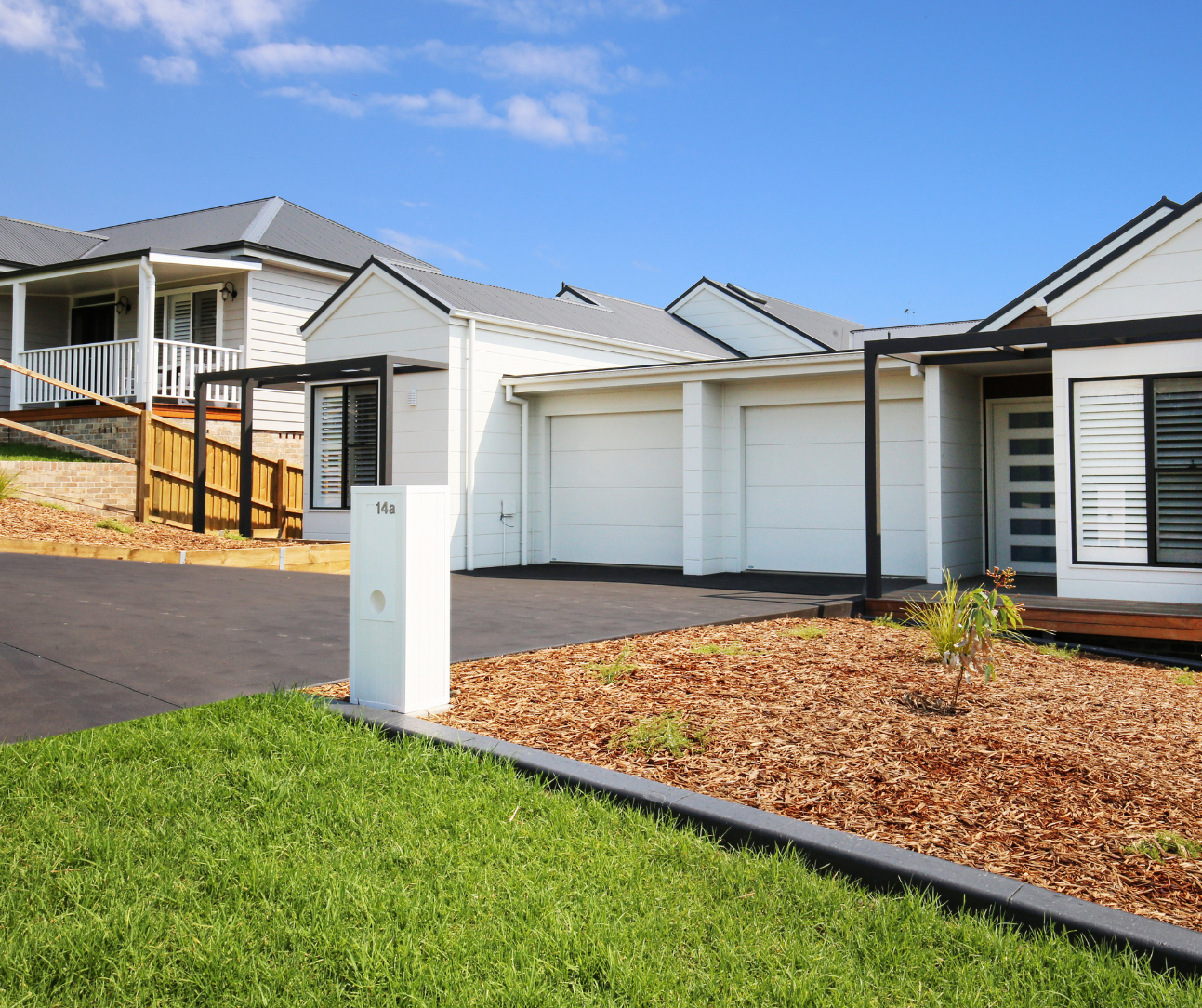 Modern suburban house exterior with white garage doors, driveway, and landscaped front yard under a blue sky