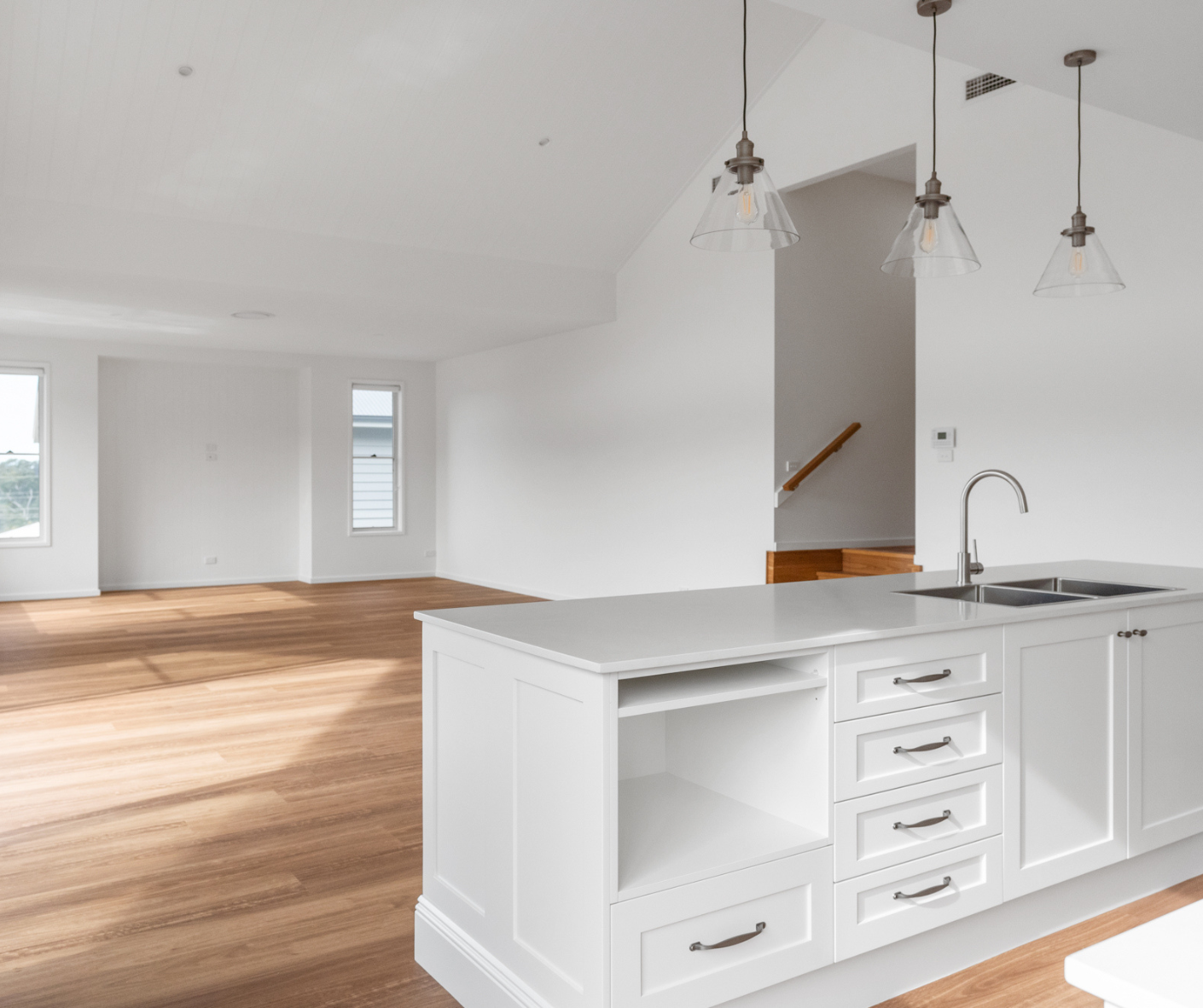 Bright open kitchen with white island, pendant lights, and hardwood floors in a modern empty room