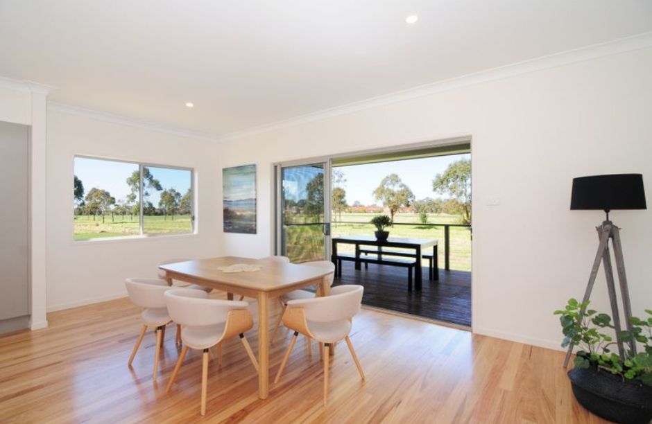 Bright dining room with wooden table, chairs, and open doors to a sunny patio and green yard