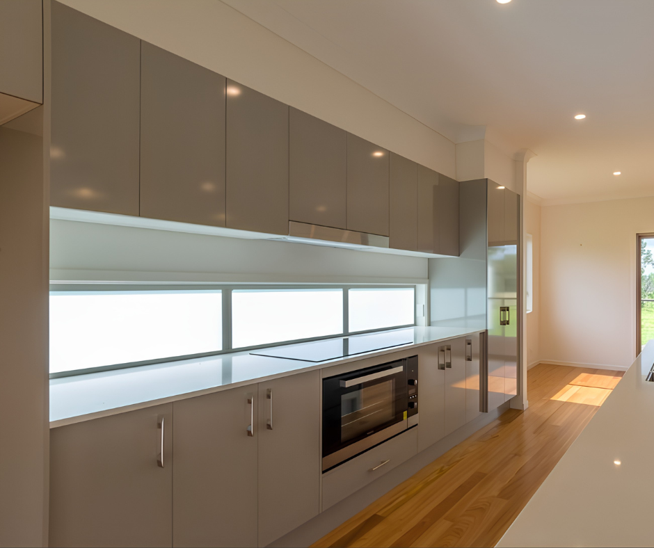 Modern kitchen with gray cabinets, white countertops, built-in oven, and wooden floor, lit by natural light