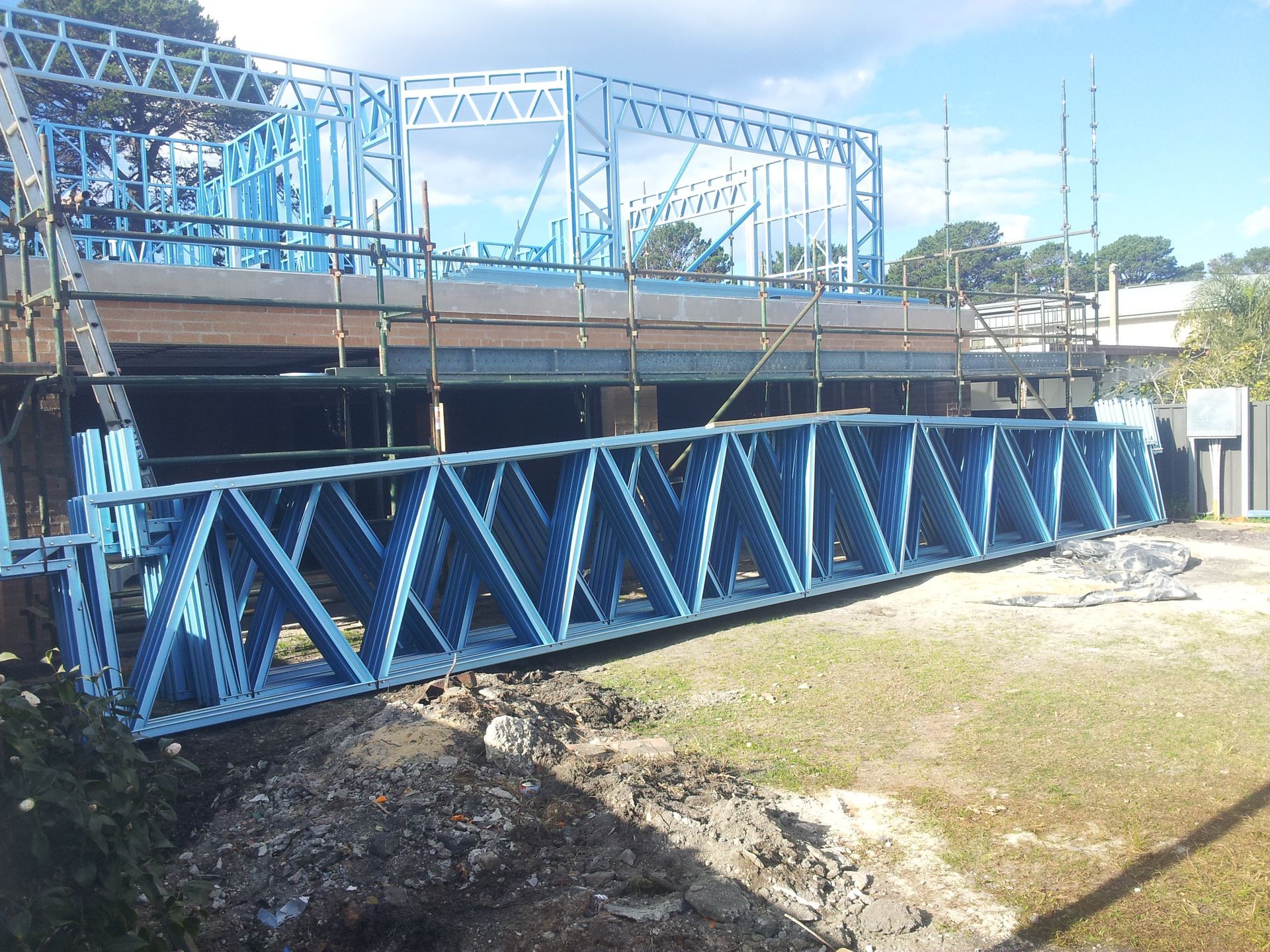 Blue metal construction framing on a construction site, with a long truss and building skeleton.